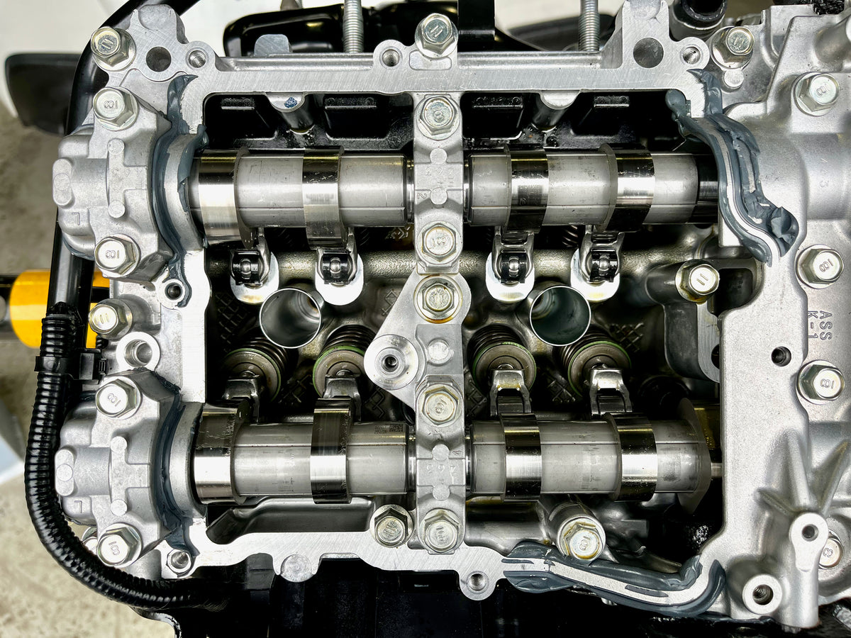 Overhead view of a Subaru FA24 cylinder head with camshafts and Denstoj FA/FB rocker retainers installed, showing the assembled valvetrain components, rocker arms, and valve springs.