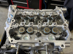 Close-up of a Subaru FA/FB cylinder head with Denstoj rocker retainer pivots installed, showing valve springs, machined aluminium head surfaces, and valvetrain components before rocker arm installation.